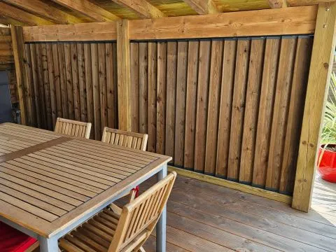 Holzterrasse mit Tisch und Stühlen vor einer Wand aus senkrechten Holzlamellen – ein einladender Außenbereich mit wohnlicher Wohlfühlatmosphäre.