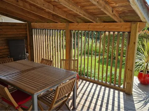 Holzterrasse mit Tisch, Stühlen und Pflanzen unter einer Überdachung mit Holzlamellen – für eine warme und gemütliche Atmosphäre.